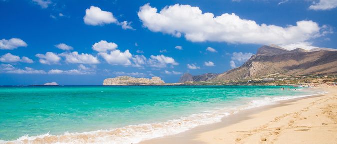 Sandstrand mit türkisfarbenem Meer, bewölktem Himmel und Bergen im Hintergrund an der Küste von Falassarna auf Kreta.