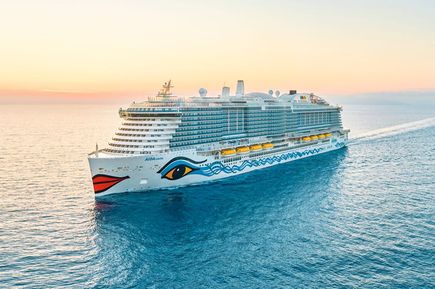 Kreuzfahrtschiff AIDAcosma fährt bei Sonnenuntergang über das ruhige Meer; gut sichtbar sind das typische AIDA-Lächeln am Bug und die moderne, mehrstöckige Bauweise