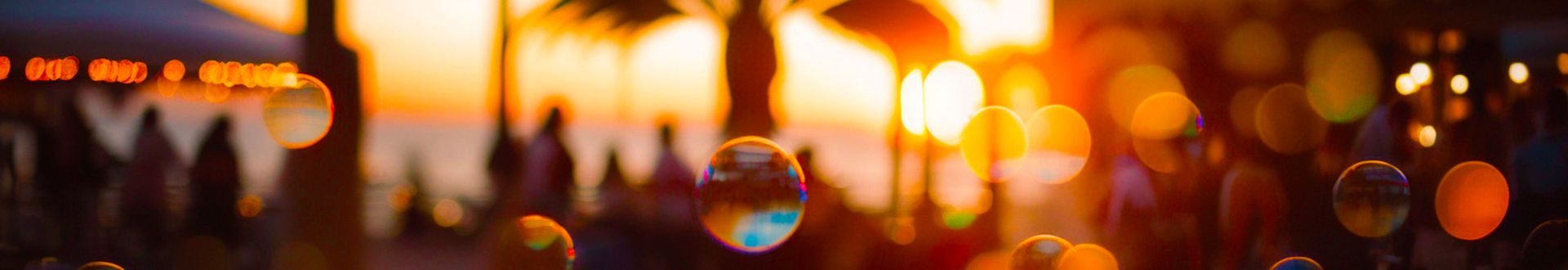 Sonnenuntergang über einer Outdoor-Party mit Palmen im Hintergrund. Seifenblasen schweben im Vordergrund.