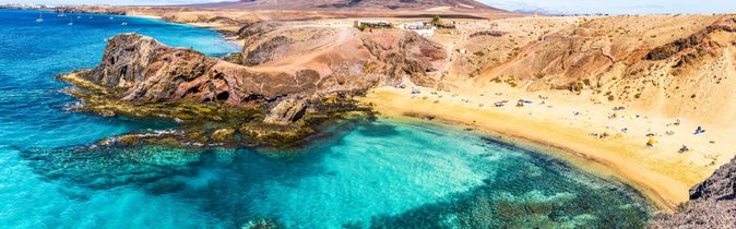 Bucht mit klarem türkisfarbenem Wasser, Sandstrand und felsiger Küste auf den Kanarischen Inseln unter blauem Himmel