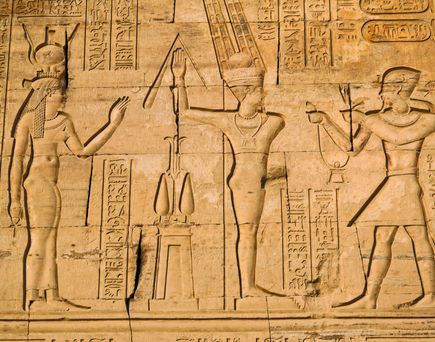 Steinrelief mit ägyptischen Hieroglyphen und Abbildungen von Göttern und Pharaonen in einer Tempelwand