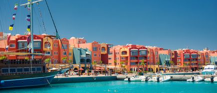 Bunte Gebäude und Boote am Hafen von Hurghada bei klarem Himmel, mit Palmen und einer lebhaften Uferpromenade