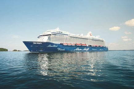 Das Kreuzfahrtschiff Mein Schiff 6 fährt bei sonnigem Wetter über ein ruhiges Gewässer und ist seitlich vollständig zu sehen.