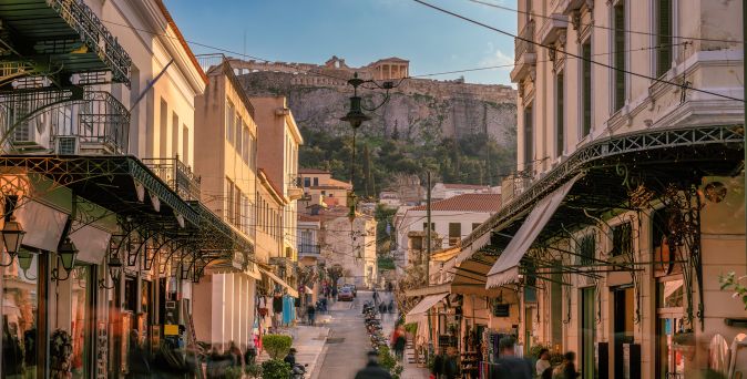 Blick auf eine belebte Straße in der Altstadt Plaka in Griechenland mit historischen Gebäuden und der Akropolis im Hintergrund.