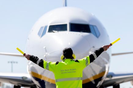Mitarbeiter des Vorfeldbetriebs am Flughafen Köln/Bonn weist ein Passagierflugzeug auf dem Rollfeld ein. Die Aufnahme zeigt die Frontansicht des Flugzeugs sowie die Bodenabfertigung und Sicherheitsabläufe am internationalen Verkehrsflughafen Köln/Bonn.