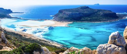 Eine breite Lagune mit leuchtend türkisfarbenem Wasser liegt zwischen hellen Sandflächen und einer flachen Felseninsel. Im Hintergrund öffnet sich das tiefblaue Meer unter einem klaren, sonnigen Himmel.