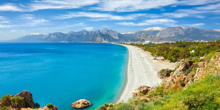Weitläufiger Blick auf den Konyaalti Beach in Antalya mit türkisblauem Meer, hellem Sandstrand und dem Taurusgebirge im Hintergrund