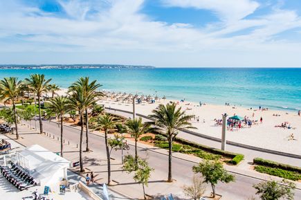 Strandpromenade an der Playa de Palma auf Mallorca mit Palmen, Sonnenschirmen und Menschen am breiten Sandstrand