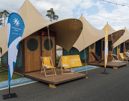 Mehrere Glamping-Zelte mit Holzterrassen und Liegestühlen auf dem Gelände des Glücksgefühle Festivals.
