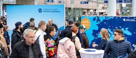 Zahlreiche Besucher informieren sich beim Flughafenfest 2025 am Stand des Albrecht Dürer Airport Nürnberg vor einer Übersichtskarte mit dem Hinweis „Nonstop Flüge im Sommer 2025!“