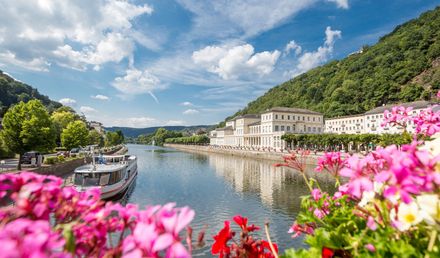 Bad Ems an der Lahn mit Flusspromenade, historischem Gebäudeensemble und Booten, eingerahmt von grünen Hügeln und Blumen