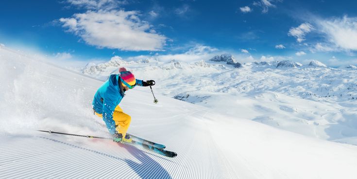 Skifahrer auf einer präparierten Piste in einem schneebedeckten Skigebiet mit weitläufiger Berglandschaft und Alpenpanorama im Hintergrund