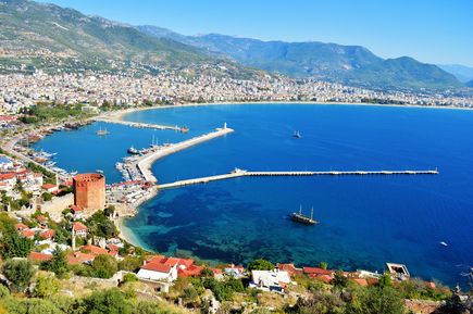 Panoramablick auf den Hafen von Alanya mit dem Roten Turm, der langen Mole, klarem Meer und der Stadt vor den Bergen