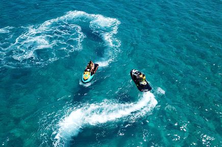Zwei Jetskis fahren über das türkisfarbene Meer und hinterlassen weiße Wasserwirbel