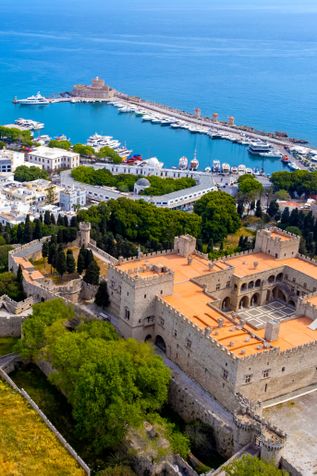 Luftaufnahme der Altstadt von Rhodos mit der mittelalterlichen Großmeisterpalastanlage im Vordergrund und dem Hafen mit Yachten im Hintergrund.