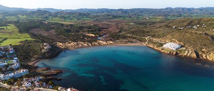 Luftaufnahme der Playas de Fornells auf Menorca mit grünen Feldern, Wäldern und einer weitläufigen Bucht mit türkisblauem Wasser