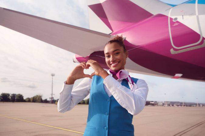 Eurowings Crew-Mitglied formt mit den Händen ein Herz vor dem Heck eines Airbus A320neo auf dem Flughafenvorfeld