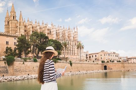 Frau mit Sonnenhut und Stadtplan vor der gotischen Kathedrale La Seu in Palma de Mallorca