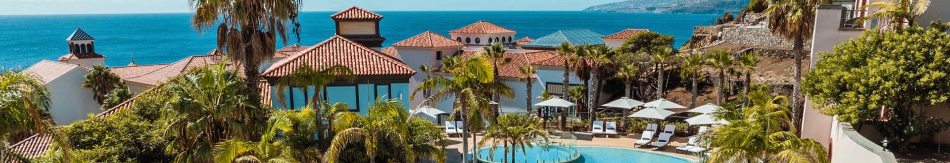 Blick auf das Dreams Madeira Resort mit Pool, Palmen, Liegestühlen und Meer im Hintergrund.