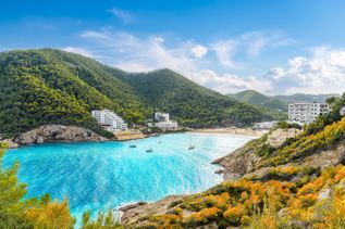 Bucht Cala Llonga auf Ibiza mit türkisblauem Wasser, Segelbooten und von grünen Bergen umgebenen Hotels