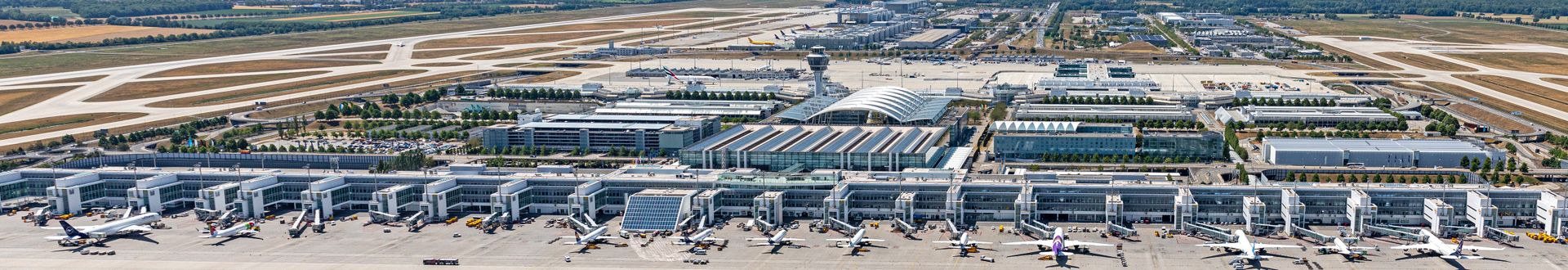 Panorama-Luftaufnahme von Terminal 2 am Flughafen München mit mehreren Flugzeugen an den Gates, Vorfeldbetrieb, Fluggastbrücken sowie dem München Airport Center und Kontrollturm im Hintergrund