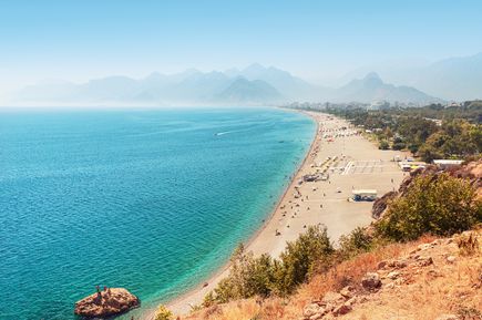 Weitläufiger Konyaaltı Beach in Antalya mit türkisblauem Meer, hellem Kiesstrand und Blick auf die umliegenden Berge