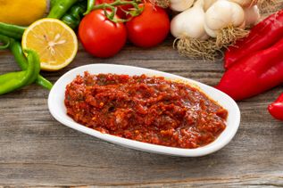Acılı Ezme, scharfer türkischer Tomaten-Paprika-Dip in weißer Schale, umgeben von frischem Gemüse