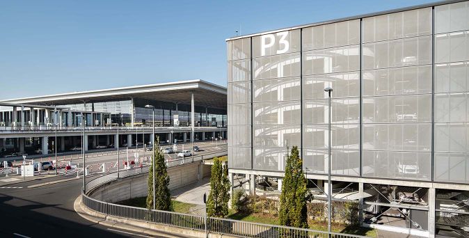 Parkhaus P3 am Flughafen BER mit sichtbarer Rampe und mehrstöckigem Gebäude, umgeben von Bäumen und Straßenlaternen.
