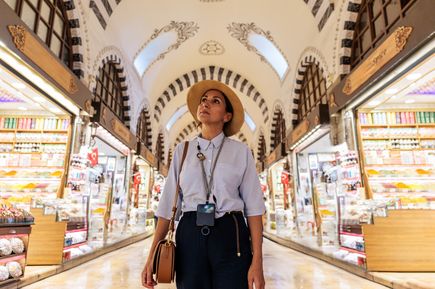 Touristin mit Hut steht im Gang des Großen Basars in Istanbul, umgeben von beleuchteten Marktständen unter einer historischen, gewölbten Decke