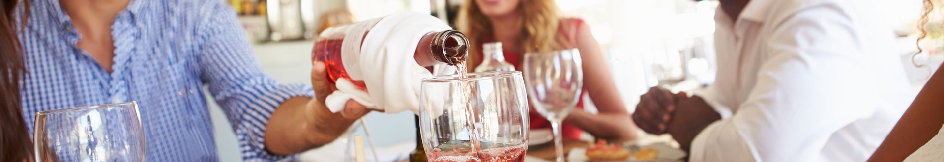 Ein Glas Roséwein wird bei einem gemeinsamen Essen am Tisch eingeschenkt, umgeben von Tellern mit frischen Speisen