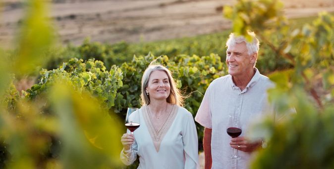 Älteres Paar genießt ein Glas Rotwein bei Sonnenuntergang inmitten eines Weinbergs