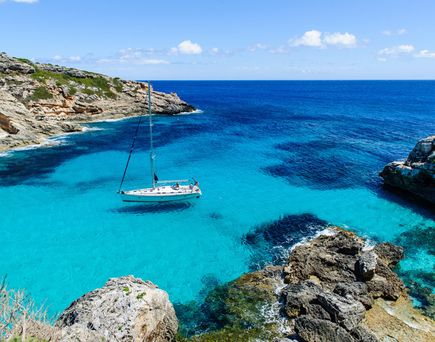 Segelboot auf klarem türkisblauem Wasser in einer felsigen Bucht unter blauem Himmel