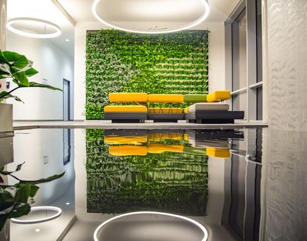 Moderne Sitzecke mit gelb-schwarzem Sofa vor einer grünen Pflanzenwand, reflektiert in einem glänzenden Boden, mit runden Deckenleuchten