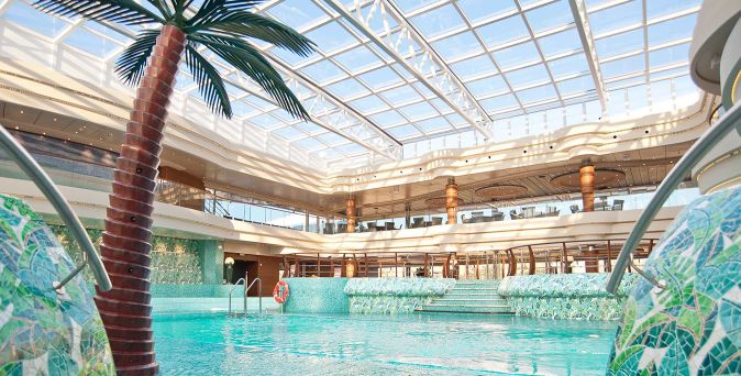 Innenpoolbereich L’Equatore auf der MSC Splendida mit großer Glasdachkonstruktion, Palmen-Dekor und türkisfarbenem Wasser
