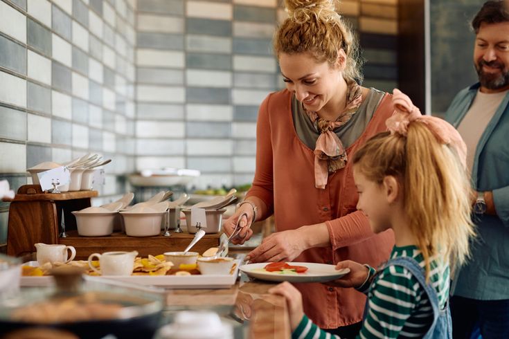Personen bedienen sich am Frühstücksbuffet im Hotel mit frischem Obst und warmen Speisen