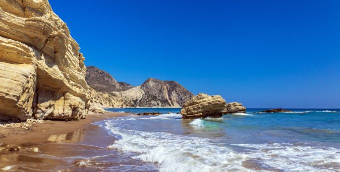 Felsige Küste mit Sandstrand und Wellen am Meer unter klarem Himmel