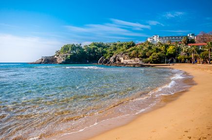 Feinsandiger Incekum Beach mit flach abfallendem Meer, sanften Wellen und grünen Hotelanlagen an der türkischen Riviera