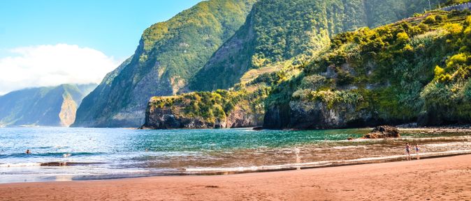 Strand Praia do Porto do Seixal auf Madeira mit Sand, türkisblauem Wasser und steilen, bewachsenen Klippen entlang der Küste
