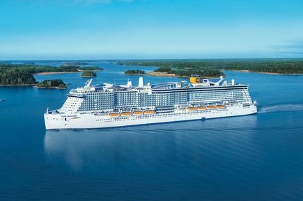 Das Kreuzfahrtschiff Costa Smeralda fährt durch eine weitläufige Meeres- und Insellandschaft; das weiße Schiff mit gelbem Costa-Schornstein und großen Balkonbereichen ist deutlich erkennbar