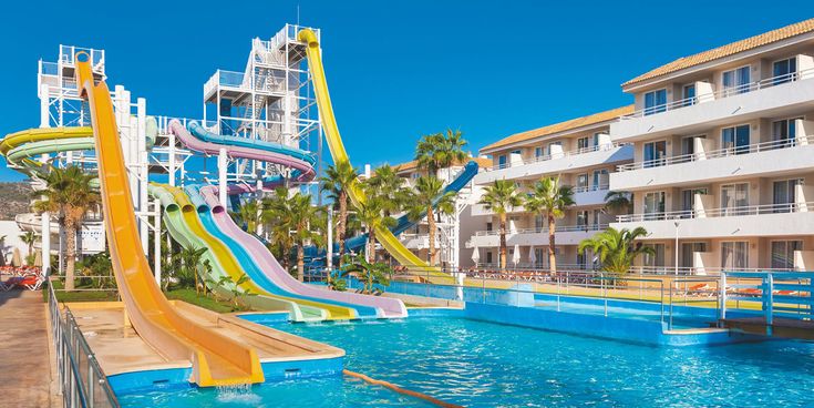 Große Hotelanlage des FERGUS Club Mallorca Waterpark mit mehreren farbenfrohen Wasserrutschen, palmengesäumtem Poolbereich und sonniger Urlaubskulisse unter klarem blauem Himmel