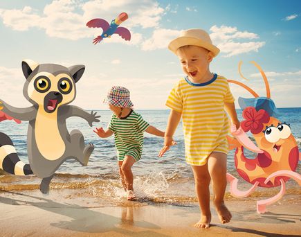 Zwei Kinder spielen lachend am Strand, umgeben von bunten Cartoon-Tieren wie einem Katta, einer Garnele und einem Papagei