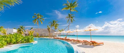 Pool mit Palmen und Sonnenschirmen neben einem Sandstrand mit Liegen und Blick auf das Meer