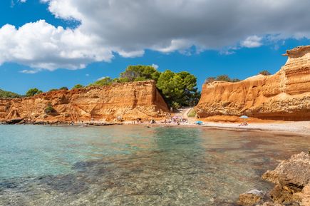 Strand Sa Caleta auf Ibiza mit roten Felsklippen, klarem Wasser und sonnenbadenden Besuchern