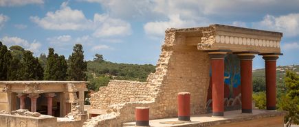 Ruinen des minoischen Palasts von Knossos auf Kreta mit farbig bemalten Säulen und Wandmalereien unter blauem Himmel mit Wolken.