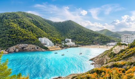 Bucht Cala Llonga auf Ibiza mit türkisblauem Wasser, grünen Hügeln und weißen Hotelanlagen am Strand