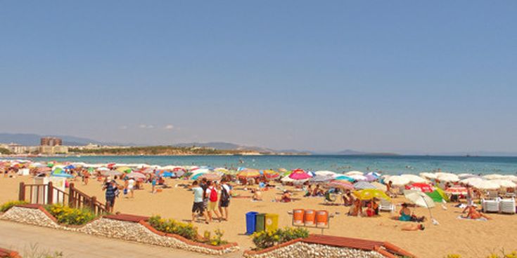 Belebter Altinkum-Strand in Didim, Türkei, mit vielen bunten Sonnenschirmen, Urlaubern am Sandstrand und Blick auf das blaue Meer unter klarem Himmel