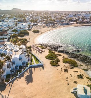 Luftaufnahme einer Bucht mit Sandstrand, Felsen und weißen Gebäuden am Ufer in einer Küstenstadt