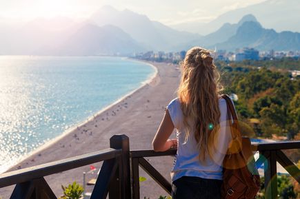 Person steht auf einer Terrasse mit weitem Blick über die Küste von Antalya in der Türkei, türkisblaues Meer und grüne Landschaft im Hintergrund