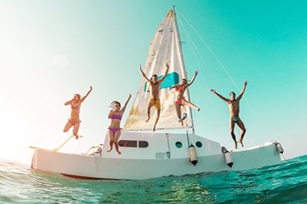 Fünf Personen springen vom Segelboot ins Meer bei klarem Himmel