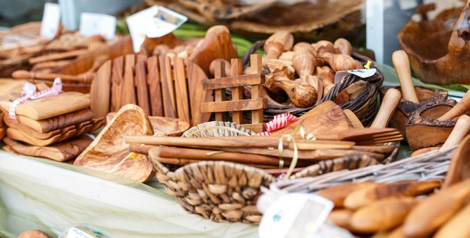 Verschiedene handgefertigte Holzartikel wie Löffel, Schalen, Schneidebretter und Gewürzhalter auf einem Marktstand.